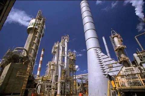 uma grande refinaria ou planta petroquímica sob um céu azul intenso. A fotografia, capturada de um ângulo baix