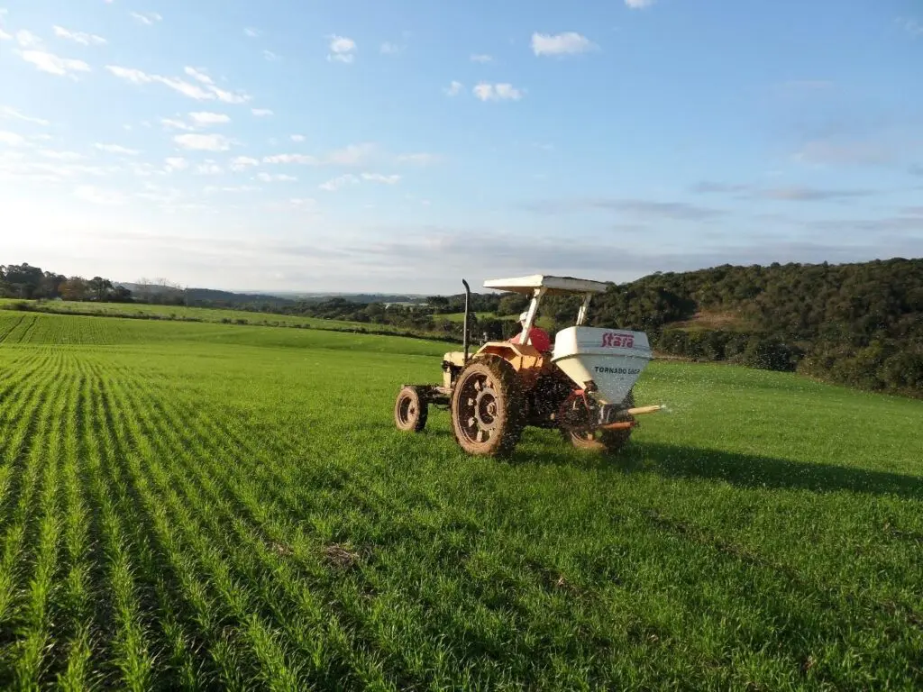operação agrícola em um dia ensolarado, com céu azul e poucas nuvens. Em primeiro plano, um trator de co