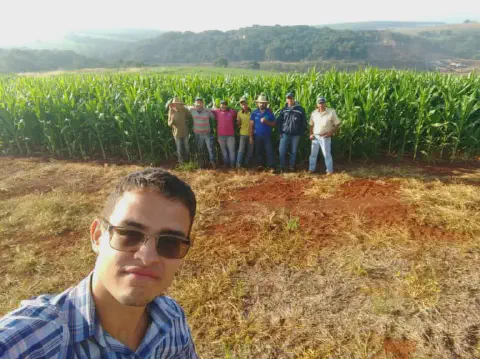 momento de confraternização e trabalho no campo. Em primeiro plano, um jovem de camisa xadrez e óculos de
