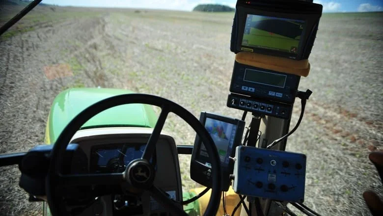 visão em primeira pessoa de dentro da cabine de um trator moderno, provavelmente da marca John Deere, evid