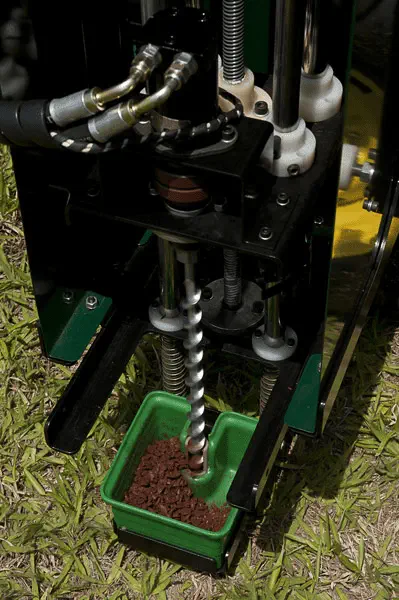 A imagem animada (GIF) exibe em close-up a operação de um amostrador de solo mecanizado. O equipamento, com estrutura metálic