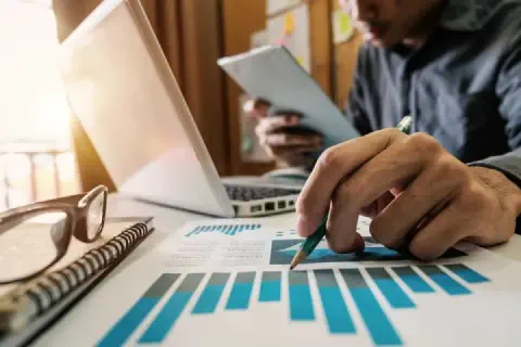 profissional em um ambiente de escritório, focado na análise de dados. Em primeiro plano, sua mão segura um