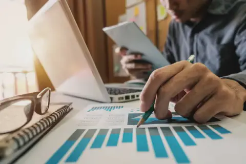 profissional em um ambiente de escritório, focado na análise de dados. Em primeiro plano, sua mão segura um