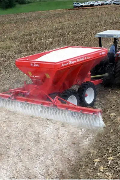 operação agrícola em pleno andamento, destacando um trator acoplado a um distribuidor de calcário vermel