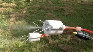 close-up de um bico de pulverização duplo, de aspecto técnico, em plena operação sobre um gramado. O dispos