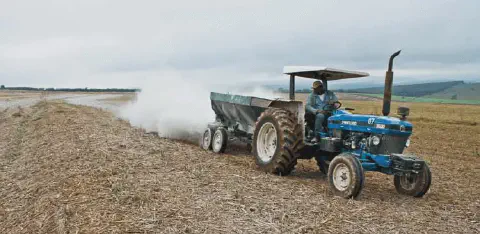 cena típica do campo, mostrando uma operação agrícola de preparo do solo. Em primeiro plano, um trator a