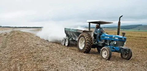 cena típica do campo, mostrando uma operação agrícola de preparo do solo. Em primeiro plano, um trator a