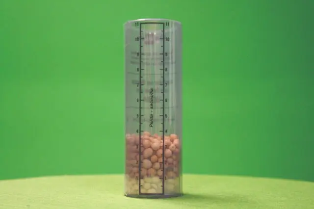 Como Medir e Reduzir Perdas na Colheita de Grãos copo medidor cilíndrico e transparente, posicionado verticalmente sobre uma superfície e contra um fundo ve