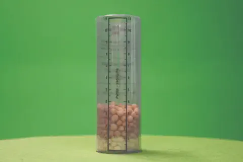 copo medidor cilíndrico e transparente, posicionado verticalmente sobre uma superfície e contra um fundo ve