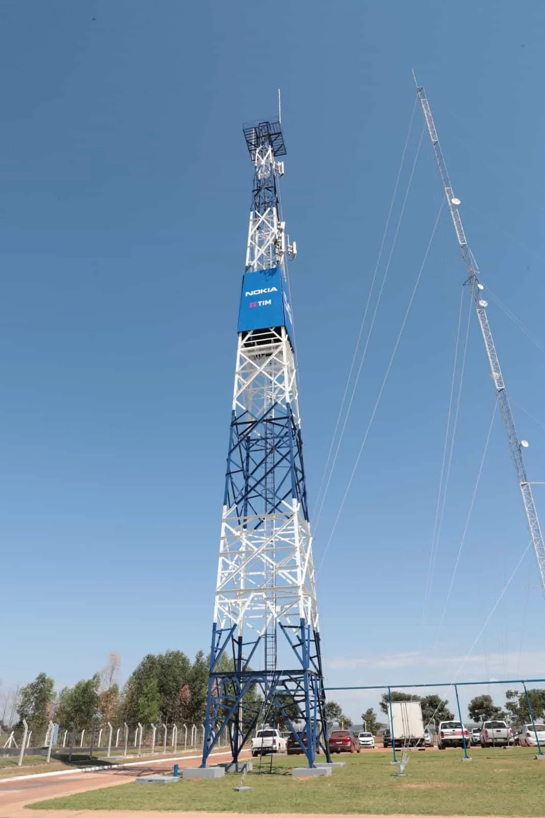 uma imponente torre de telecomunicações, pintada em azul e branco, destacando-se contra um céu azul claro e se