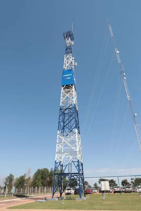 uma imponente torre de telecomunicações, pintada em azul e branco, destacando-se contra um céu azul claro e se
