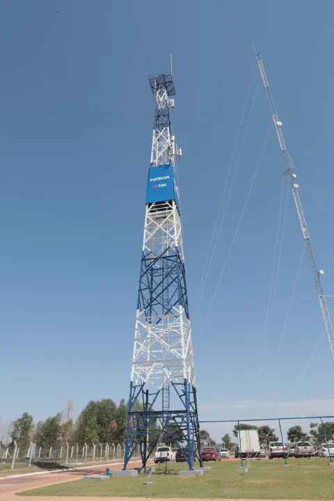 uma imponente torre de telecomunicações, pintada em azul e branco, destacando-se contra um céu azul claro e se
