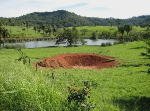 uma paisagem rural brasileira, caracterizada por colinas cobertas de pastagem verdejante sob um céu claro. Em