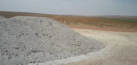 uma grande pilha de calcário agrícola, um corretivo de solo essencial, depositada na beira de uma vasta área d