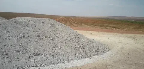 uma grande pilha de calcário agrícola, um corretivo de solo essencial, depositada na beira de uma vasta área d