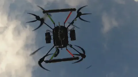 drone agrícola, especificamente um octocóptero, em pleno voo, visto de um ângulo inferior contra um céu a