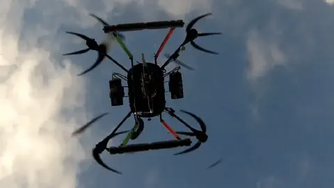 drone agrícola, especificamente um octocóptero, em pleno voo, visto de um ângulo inferior contra um céu a
