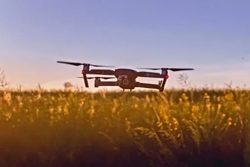 drone quadricóptero moderno em voo baixo sobre uma lavoura com flores amarelas, provavelmente colza ou um