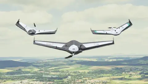 três drones de asa fixa, conhecidos como VANTs (Veículos Aéreos Não Tripulados), em pleno voo sobre uma vasta