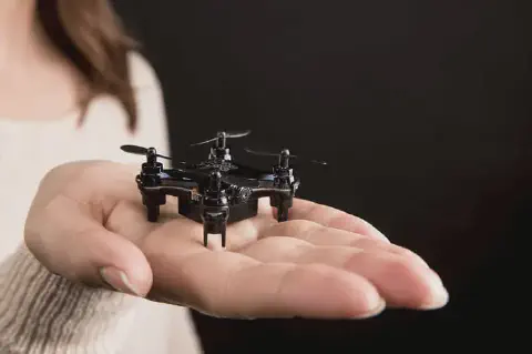 close-up da mão de uma pessoa segurando um pequeno drone preto, também conhecido como mini drone ou nano dr