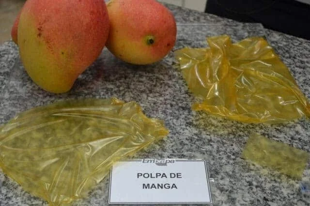 uma bancada de granito onde estão dispostas duas mangas frescas e um material inovador derivado da fruta. Em p