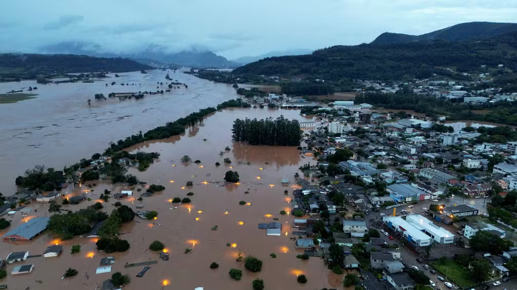 vista aérea desoladora de uma cidade severamente inundada, provavelmente no sul do Brasil, dado o relevo. Um r