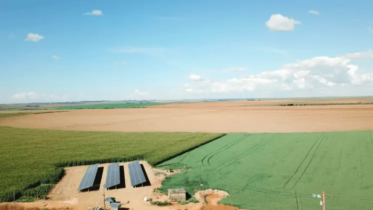 Energia Solar no Campo: Sustentabilidade na Agricultura uma ampla paisagem rural sob um céu azul e ensolarado, capturada de uma perspectiva aérea. Em primeiro plano,