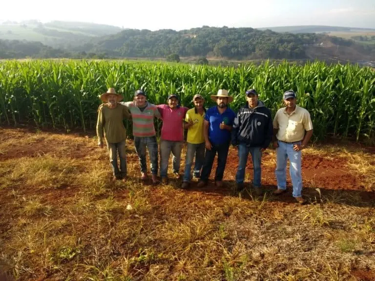 grupo de sete agricultores posando juntos, com um semblante de satisfação e orgulho, em frente a uma exte