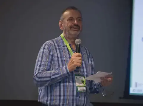 homem de meia-idade, com barba e cabelo curto, durante uma apresentação em um evento profissional, possiv