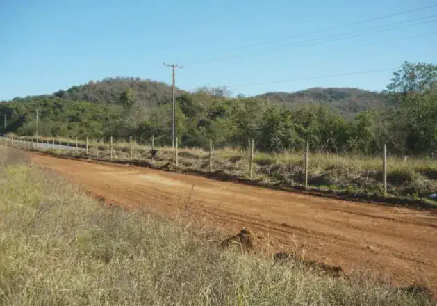 Estrada de Terra e Cerca em Propriedade Rural no Brasil uma paisagem rural sob um céu azul e limpo. Em destaque, uma estrada de terra batida, de coloração avermelhada
