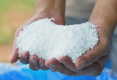 close-up das mãos de uma pessoa, possivelmente um agricultor ou agrônomo, segurando uma quantidade de ferti