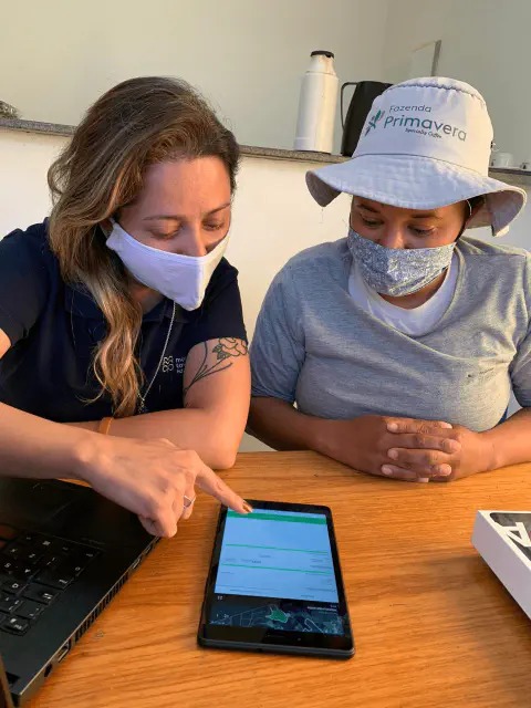 duas mulheres em um ambiente de trabalho, provavelmente em uma fazenda, sentadas a uma mesa de madeira. Uma