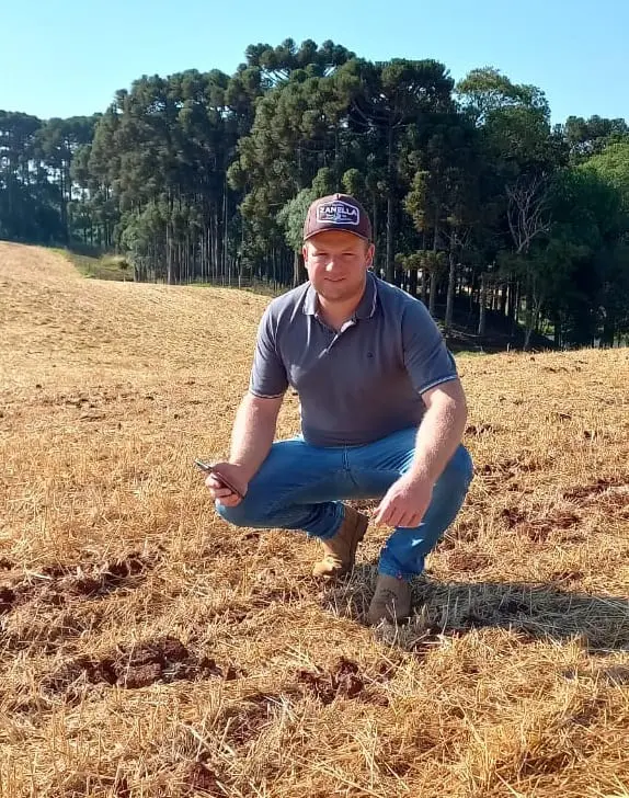 Gestão da lavoura com tecnologia na palma da mão produtor rural ou agrônomo agachado em um campo agrícola após a colheita, que está coberto por palhada se