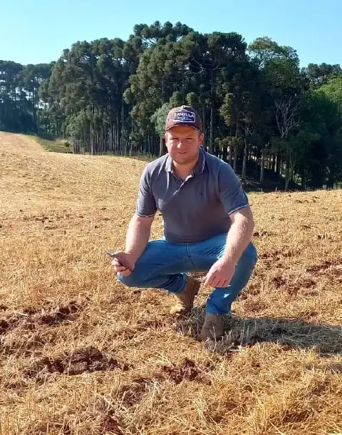 produtor rural ou agrônomo agachado em um campo agrícola após a colheita, que está coberto por palhada se