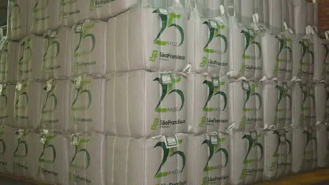 grande depósito com dezenas de big bags (sacos de grande volume) brancos, empilhados de forma organizada em