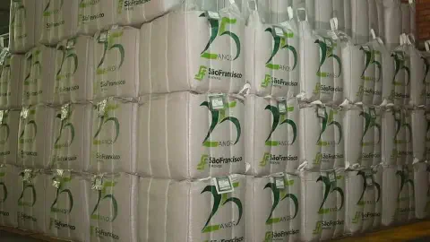 grande depósito com dezenas de big bags (sacos de grande volume) brancos, empilhados de forma organizada em