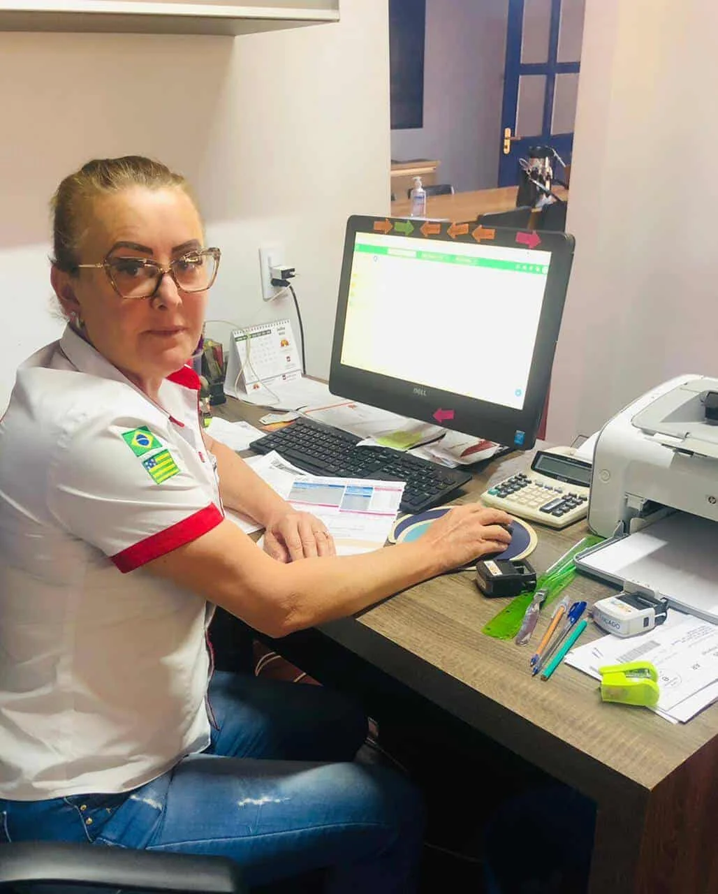 mulher de meia-idade em um ambiente de escritório, sentada em sua mesa de trabalho. Ela veste uma camisa