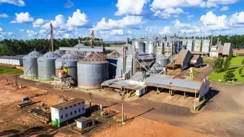 Vista aérea de um grande complexo agroindustrial destinado à armazenagem e beneficiamento de grãos. A imagem exibe múltiplos