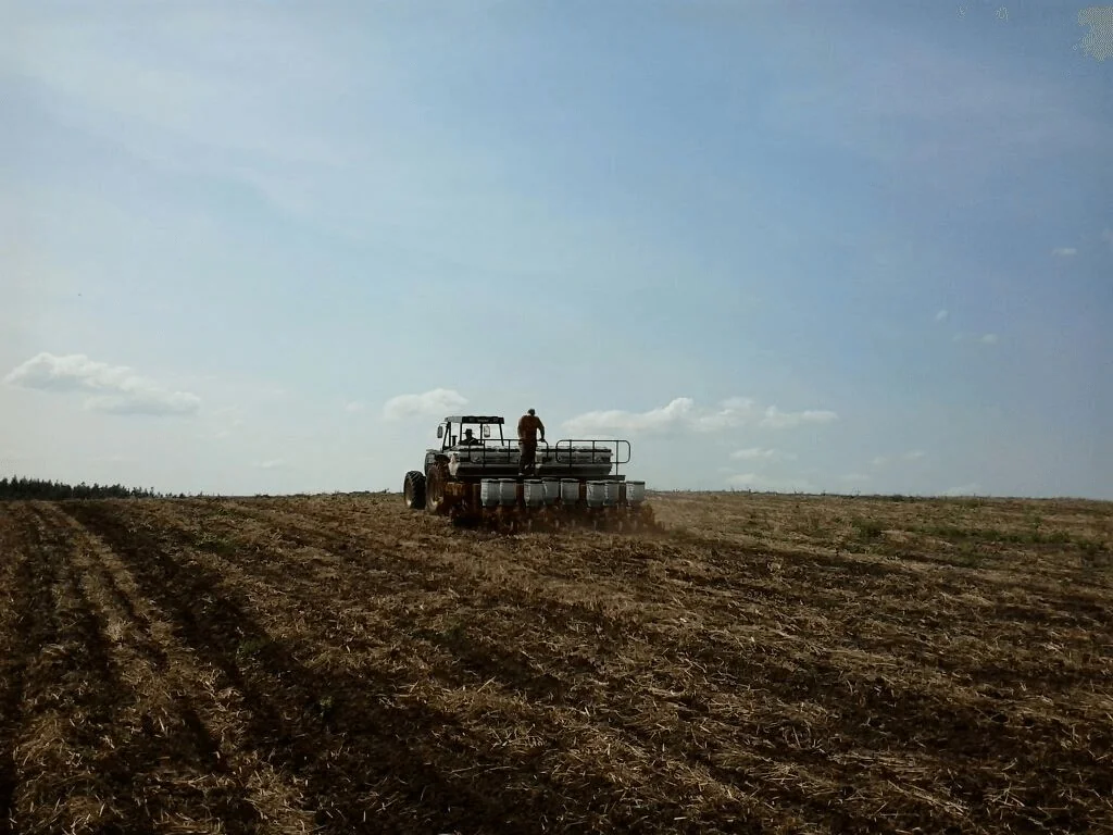 cena de campo aberto durante uma operação agrícola crucial: o plantio. Em primeiro plano, vemos um vasto