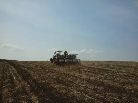 cena de campo aberto durante uma operação agrícola crucial: o plantio. Em primeiro plano, vemos um vasto
