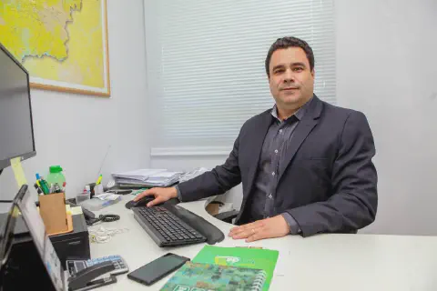 homem de meia-idade em um ambiente de escritório, sentado à sua mesa de trabalho. Ele está vestido de for