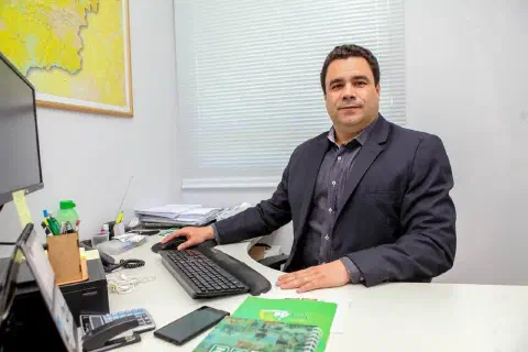 homem de meia-idade em um ambiente de escritório, sentado à sua mesa de trabalho. Ele está vestido de for