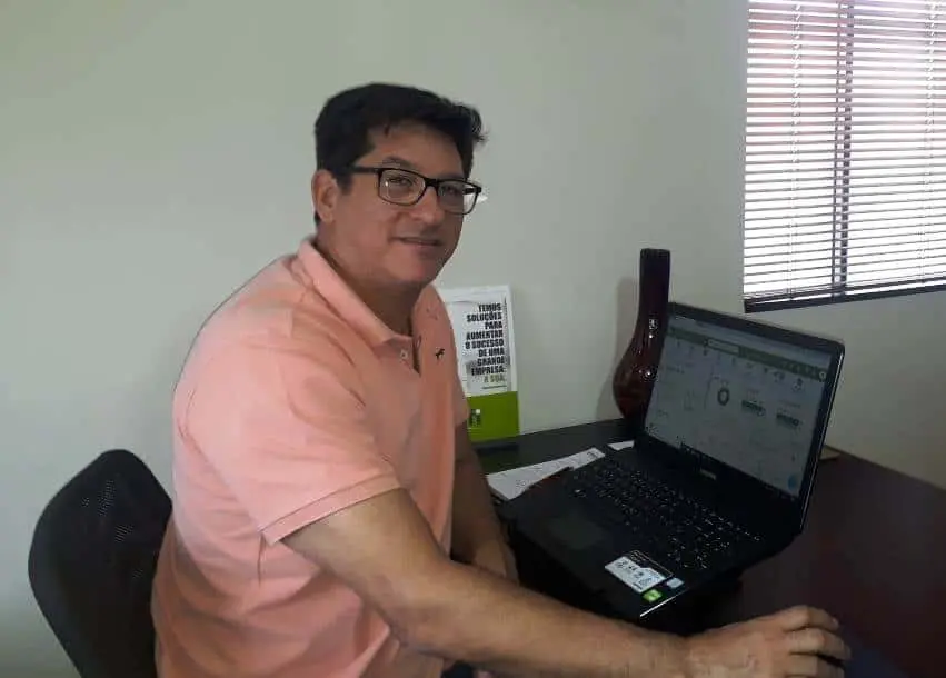 Gestor rural usando software para gestão agrícola homem de meia-idade, com óculos e camisa polo de cor salmão, sentado em sua mesa de trabalho em um ambien