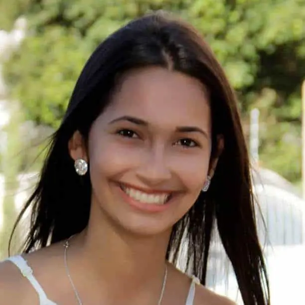 retrato em close-up de uma jovem mulher sorrindo calorosamente para a câmera. Ela possui cabelos longos e escur