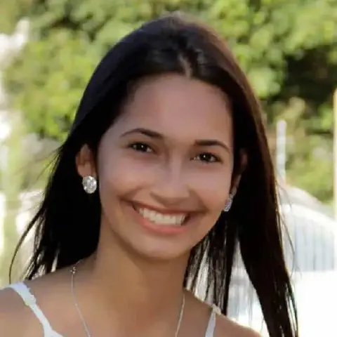 retrato em close-up de uma jovem mulher sorrindo calorosamente para a câmera. Ela possui cabelos longos e escur