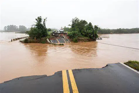 cenário devastador de uma inundação em uma área rural. Em primeiro plano, vemos a borda quebrada de uma e