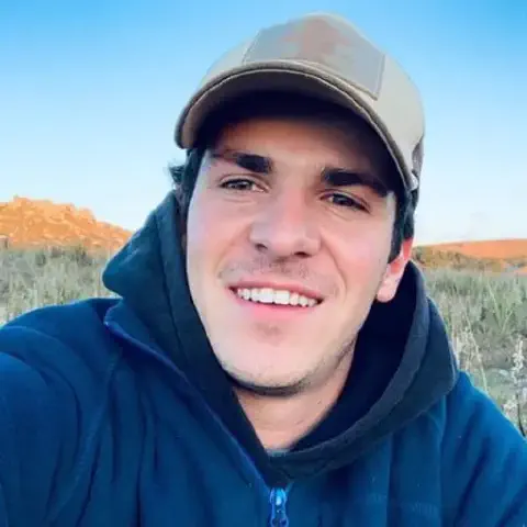 retrato em close-up de um jovem, possivelmente um produtor rural ou agrônomo, em um ambiente externo. Ele sorri
