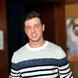 retrato em close-up de um jovem adulto do sexo masculino, sorrindo de forma amigável e confiante para a câmera.