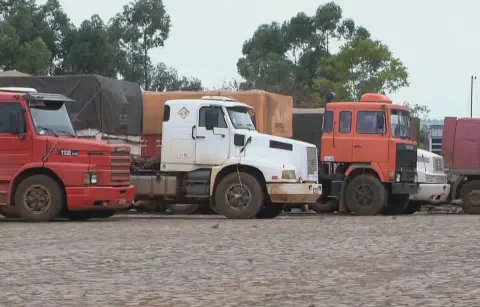 uma fileira de caminhões de grande porte estacionados em um pátio de terra ou paralelepípedos. Em primeiro pla