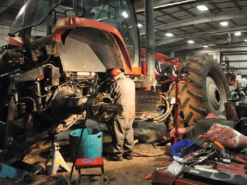 mecânico profissional realizando a manutenção de um grande trator agrícola vermelho dentro de uma oficina